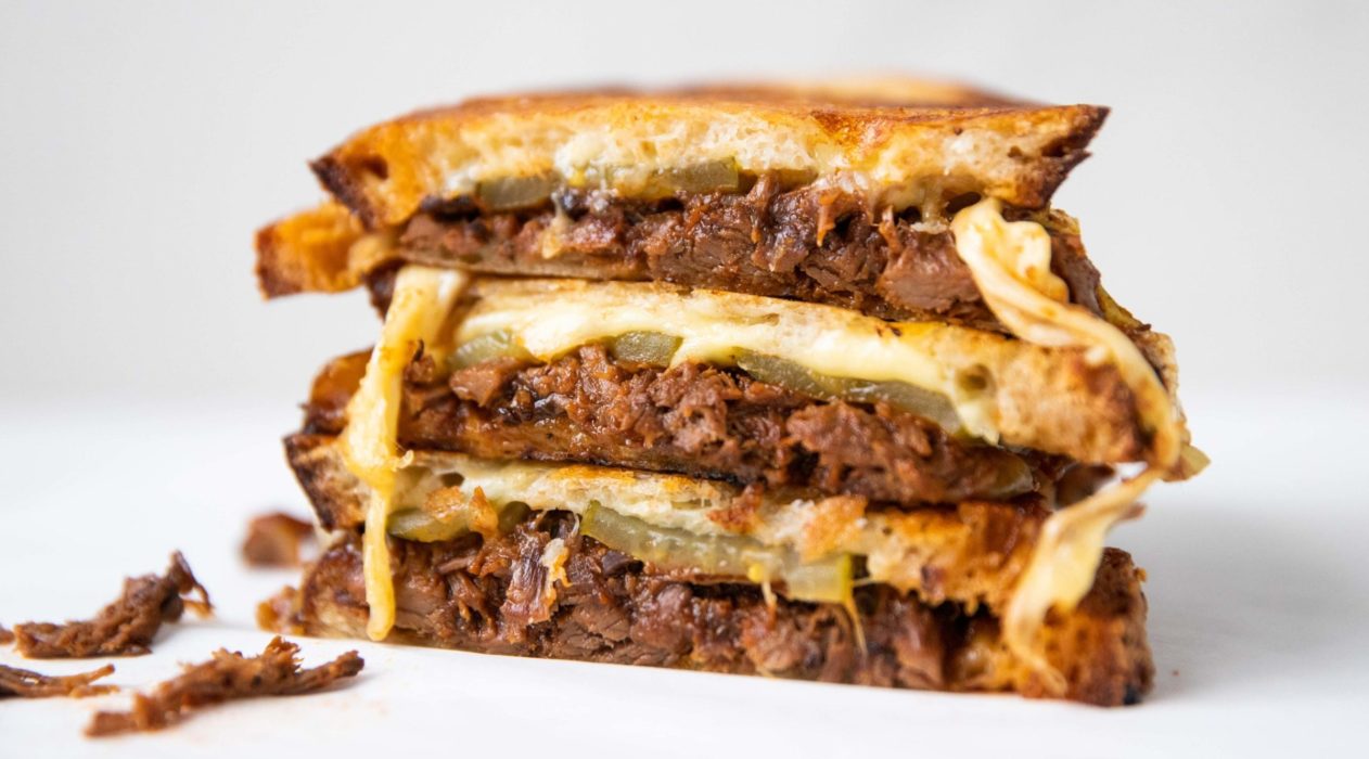 3 Beef and cheese toasties stack together on white background with a little beef spilling.