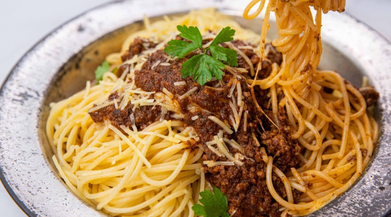 Spaghetti bolognese on a round metal plate with herb, some pasta being picked up.