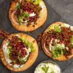 3 round bread topped with white sauce, mince, lettuce and red berries on stone board..