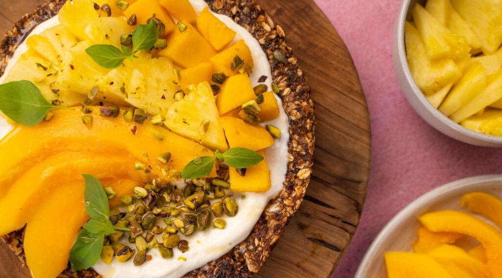 Yellow tropical fruit and green herb on granola disc on wooden board.