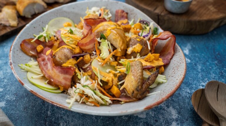 chicken and bacon on top of salad with orange sauce in a large bowl on blue table