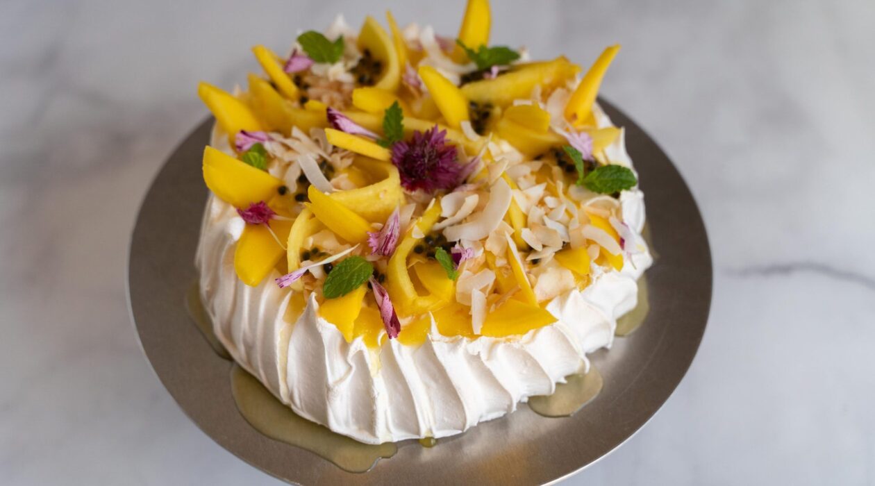 A large white cake topped with yellow fruit, red, white and green foods on a golden plate on marble.