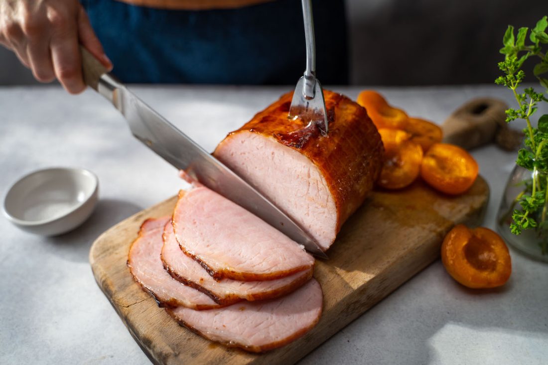 An apricot glazed ham being sliced on a wooden board