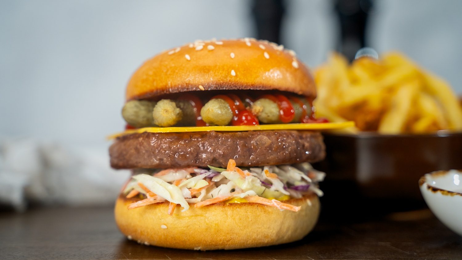 A Cheeseburger on wooden board with onion rings behind.