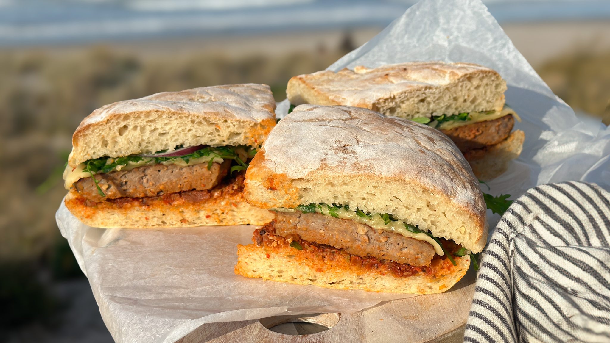 Three sandwiches on a tray showing burger filling. Beach background.