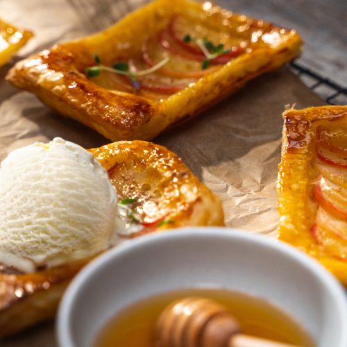 Upside down apple tarts on a cooling rack with a scoop of vanilla ice cream and a bowl of honey