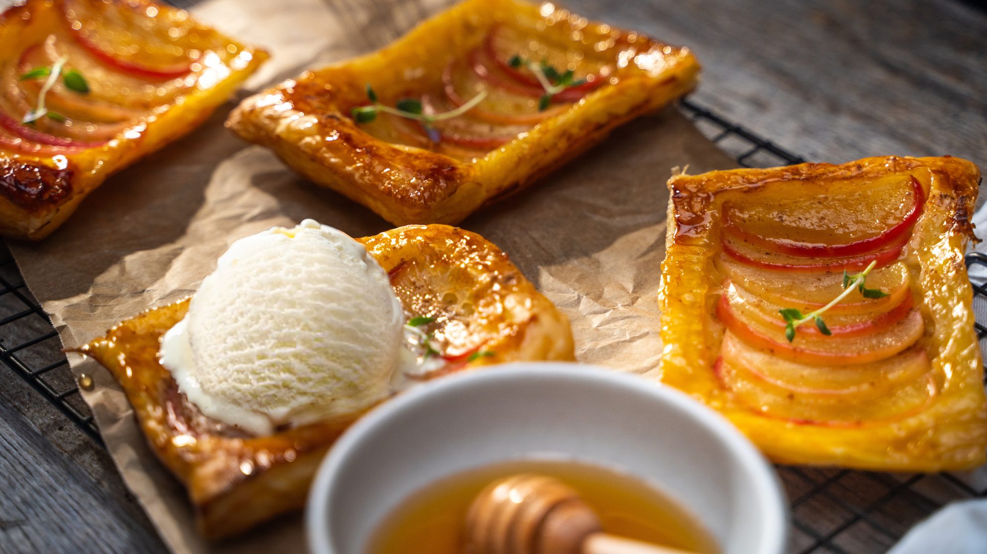 Upside down apple tarts on a cooling rack with a scoop of vanilla ice cream and a bowl of honey