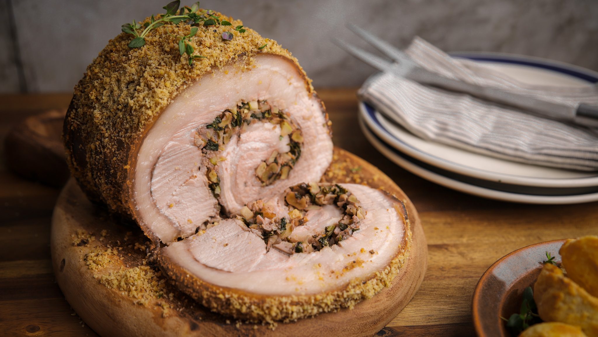 Roasted crumbed rolled pork filled with nutty crumbs on a board, sliced showing inside.