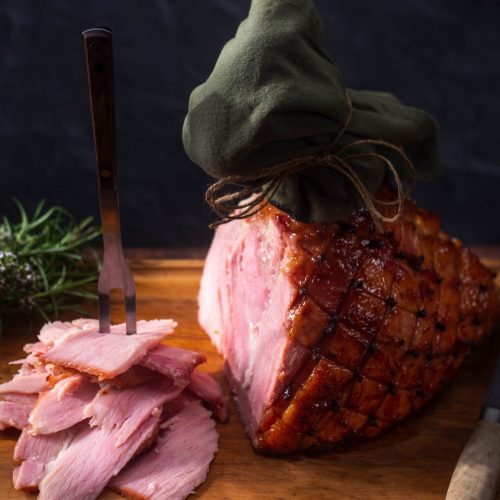 Baked whole leg ham with some sliced pieces on a wooden board.