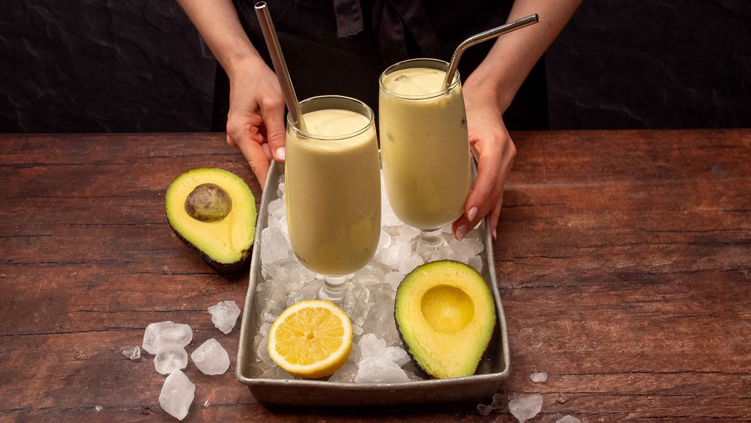 Two glasses of creamy drinks on iced tray with lemon and avocado halves.