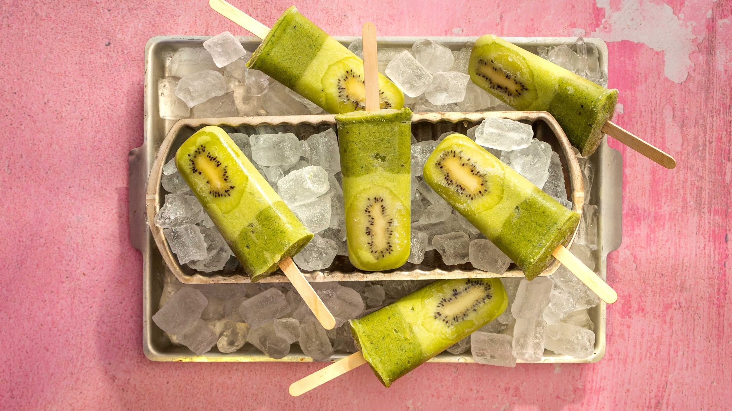 Green rectangle popsicles on cubes of ice on a tray.