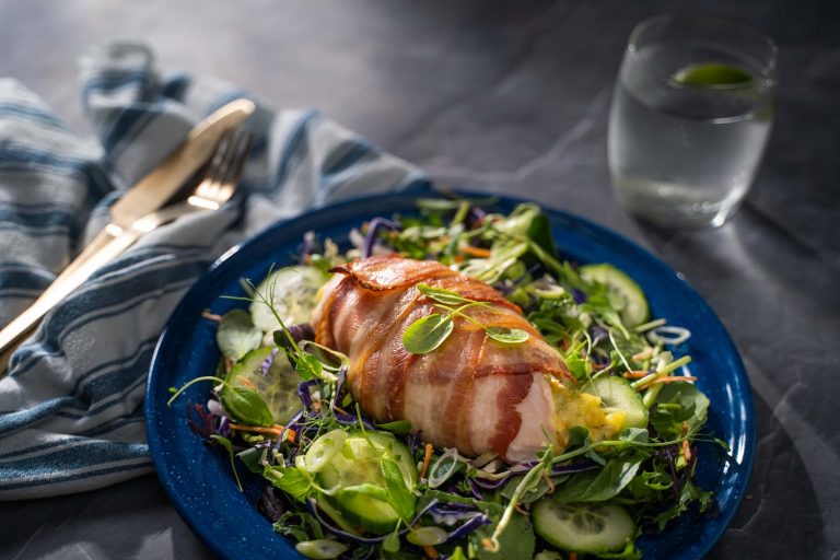 Bacon wrapped chicken breast on green salad on a blue plate, glass of water and knife and fork