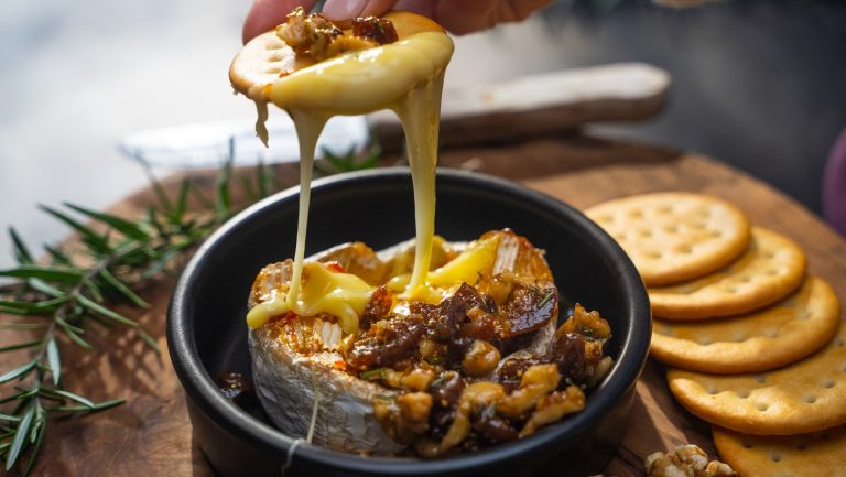 Scooping melting cheese from a black dish with a round cracker.