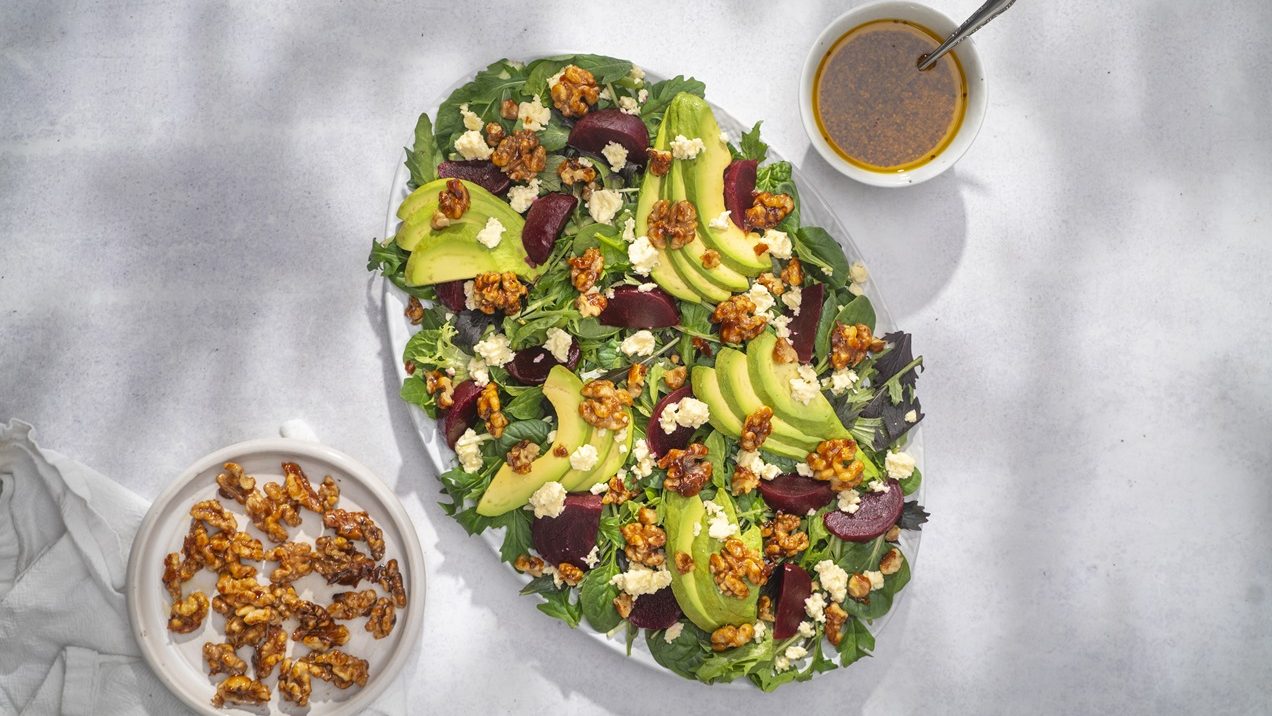 An oval plate of beetroot, avocado and walnut salad, a small plate of walnut and a bowl of dressing.