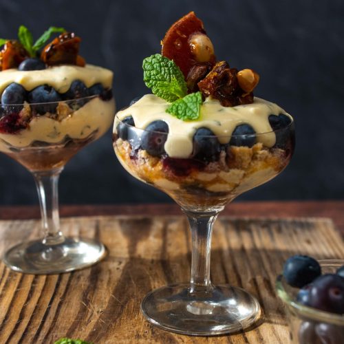 Two cocktail glasses full of creamy dessert topped with nuts and blueberries.