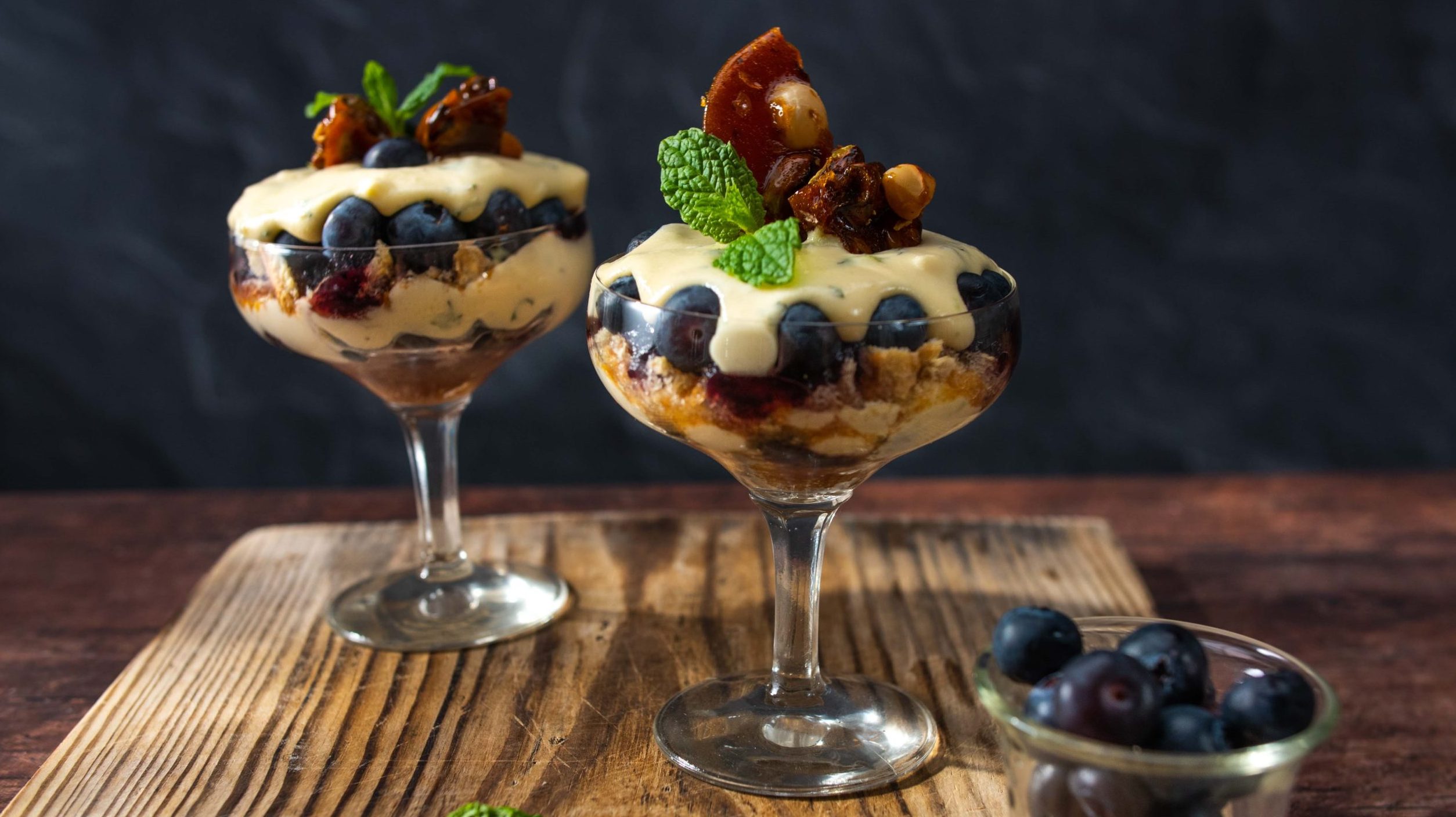Two cocktail glasses full of creamy dessert topped with nuts and blueberries.