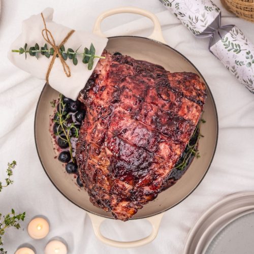 Gorgeous glazed Christmas ham in a large dish on a bed of blueberries served with fresh mint and thyme.