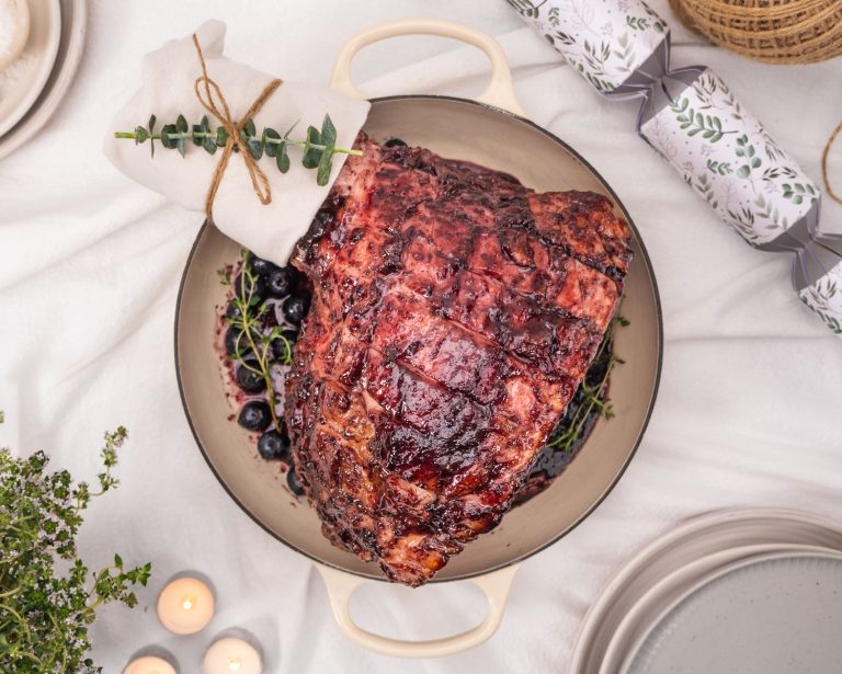Gorgeous glazed Christmas ham in a large dish on a bed of blueberries served with fresh mint and thyme.