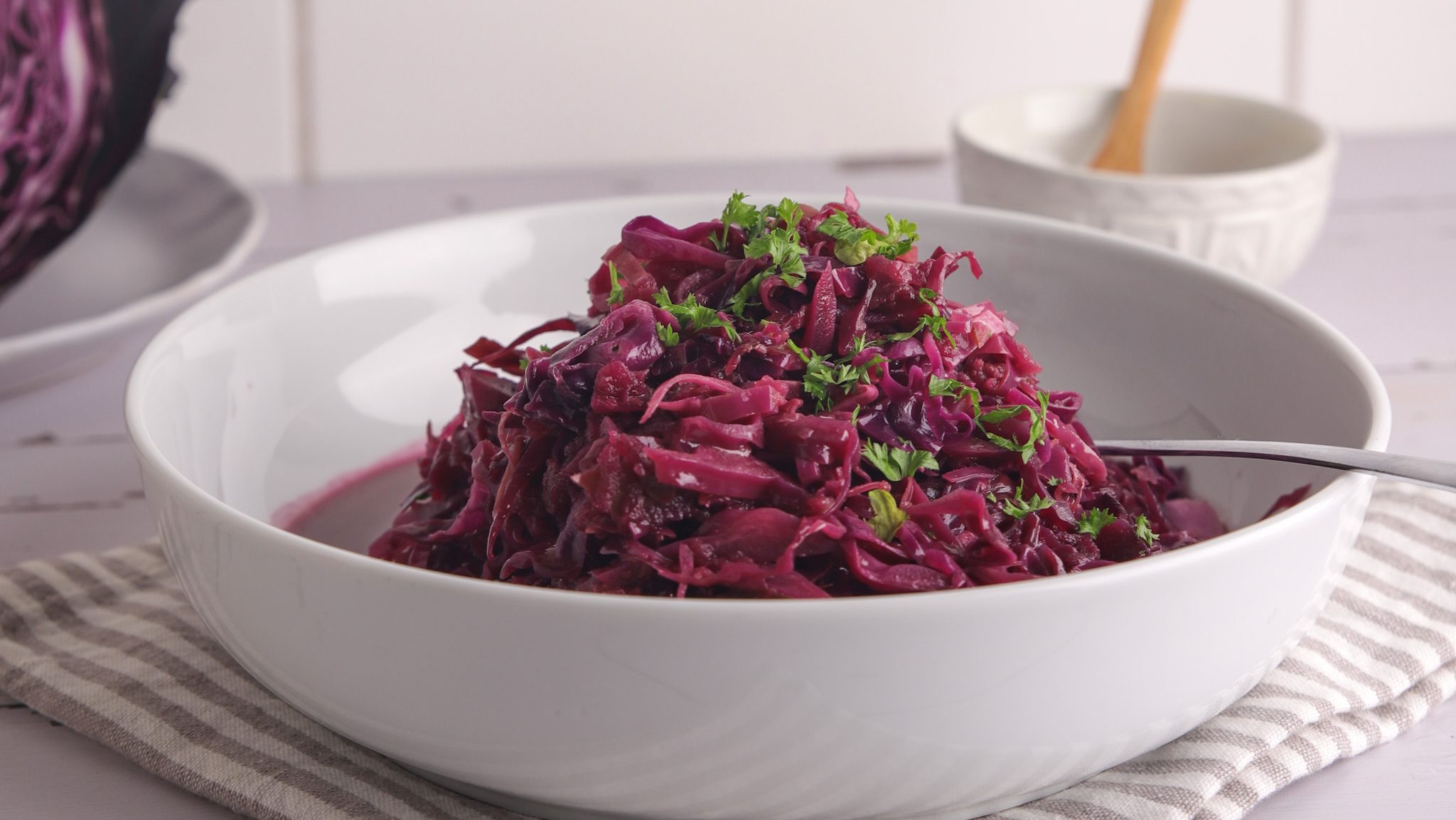 A bowl of cooked red cabbage with green herbs. A small dish of salt with spoon.