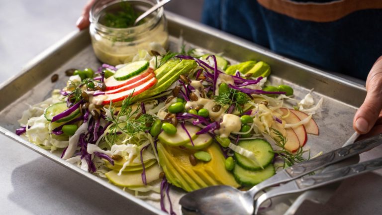 Cabbage, apple, and avocado salad with dressing on a tin tray
