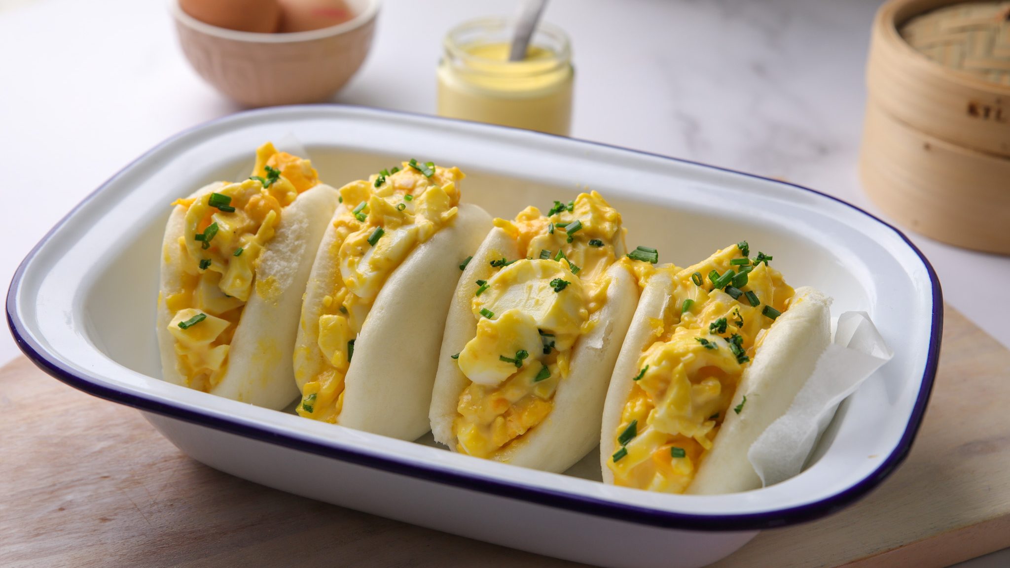 Four egg salad filled bao buns in a rectangle white bowl.