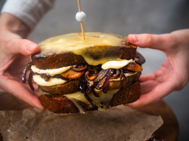 Hands holding a burger melt with mushrooms and melted cheese.