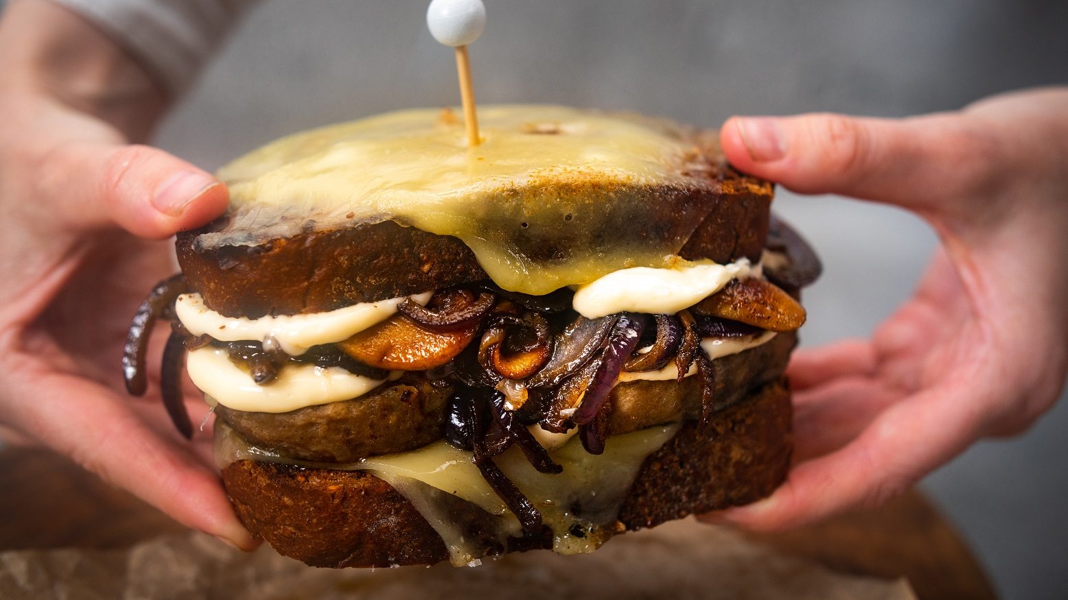 Hands holding a burger melt with mushrooms and melted cheese.