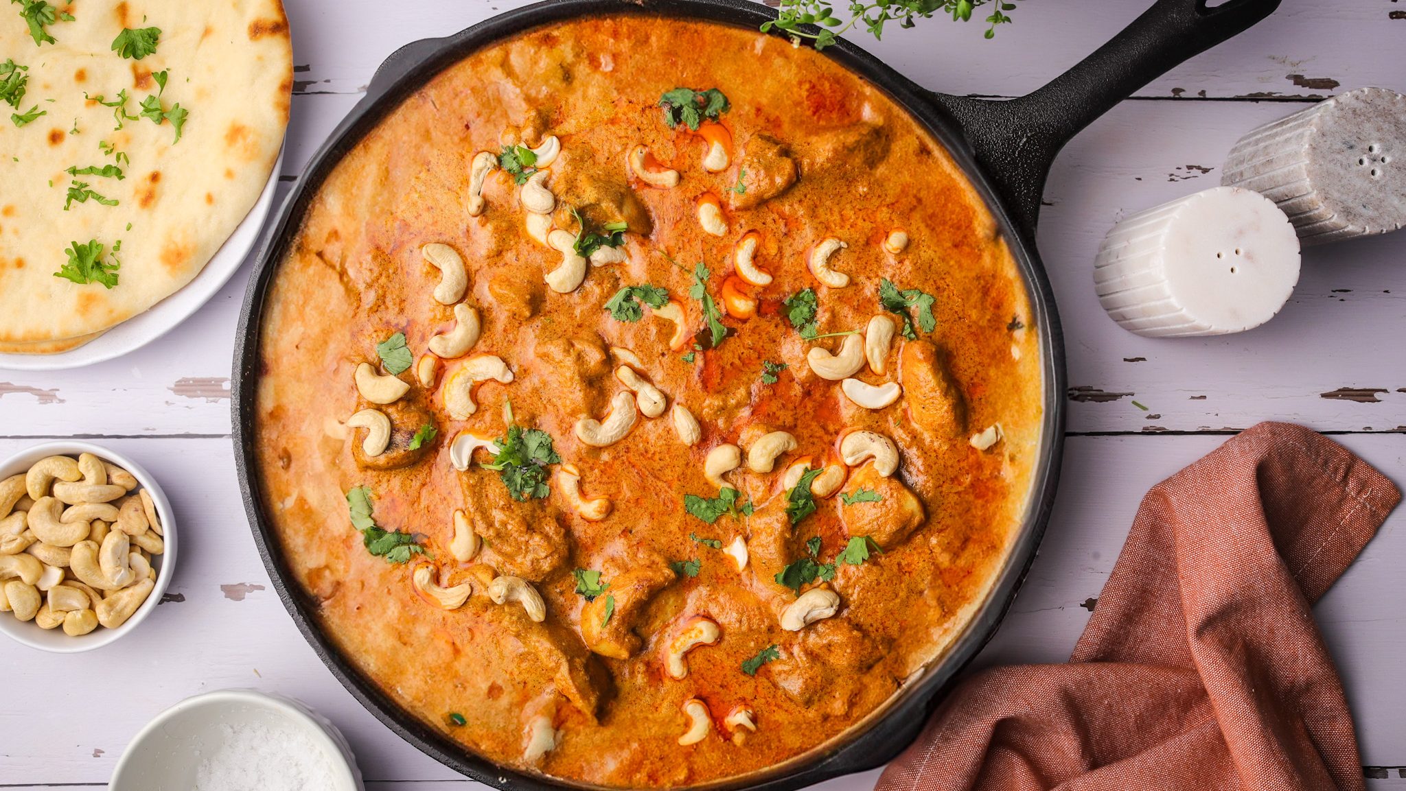 A skillet full of red curry sauce with cashews and herbs sprinkled.