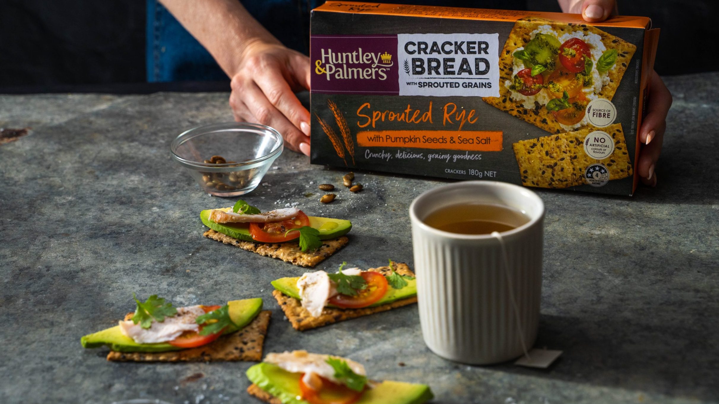 Huntley Palmers CrackerBread with chicken, avocado and tomato topping on a dark benchtop