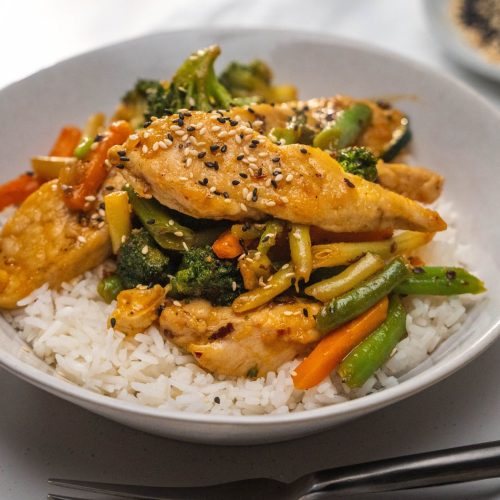 Chicken and vegetable stir-fry on white rice in a white bowl.