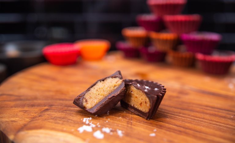 A nut-free peanot butter cup-shaped sweet snack with a chocolate coat, cut in half on a wooden chopping board.