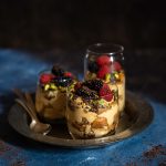 3 berry tiramisu glasses with spoons on a plate on a dark blue background
