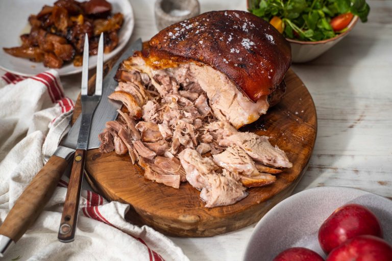 Cooked pork joint shredded on wooden board with knife and fork, apples in front