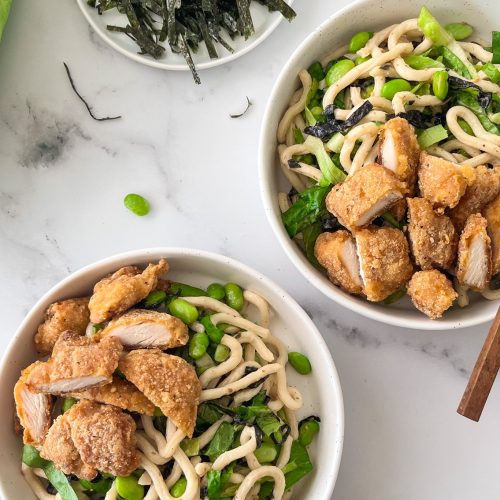 Two bowles of white noodles with cooked chicken and edamame beans, two pairs of chopsticks.