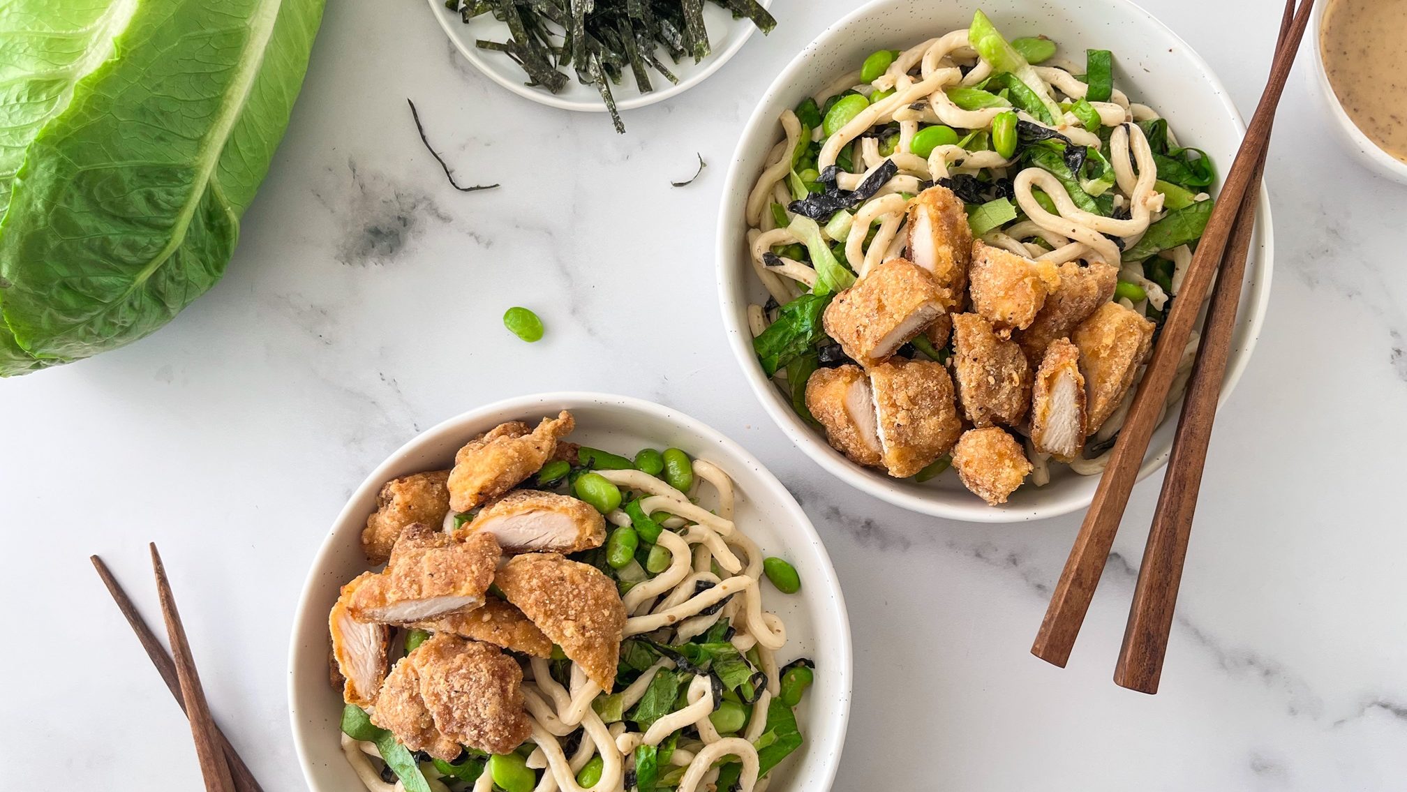 Two bowles of white noodles with cooked chicken and edamame beans, two pairs of chopsticks.