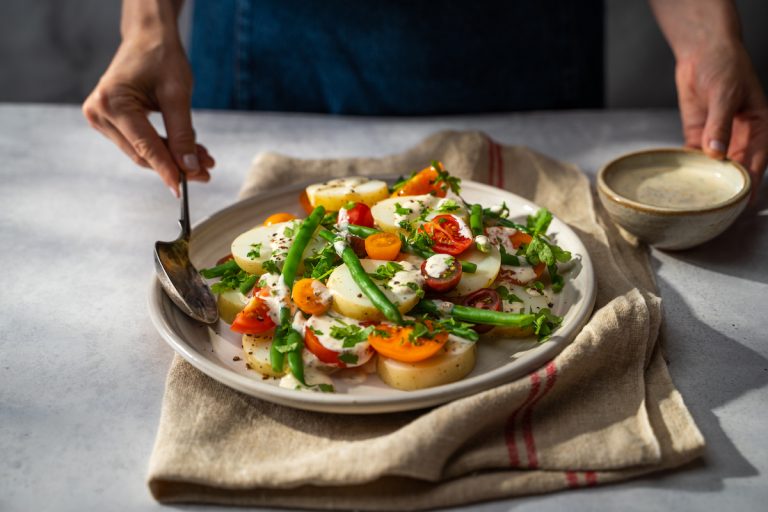 Creamy Lotatoes, tomato and green bean salad with serving spoon.