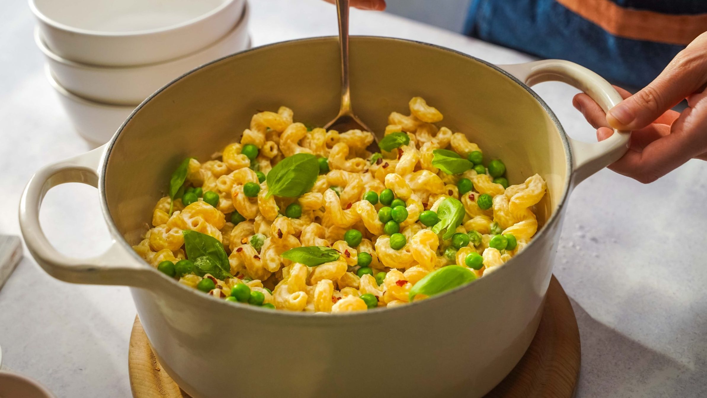 A pot of cream coloured pasta with peas, basil, and a spoon scooping.