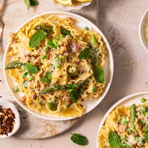 Two bowls of white pasta with asparagus spears and herbs. Lemon and chilli.