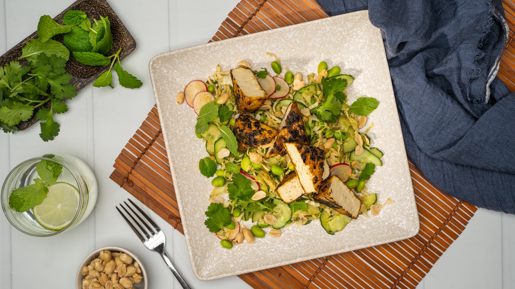 A birds eye vewi of a salad on square plate, with greens and tofu.