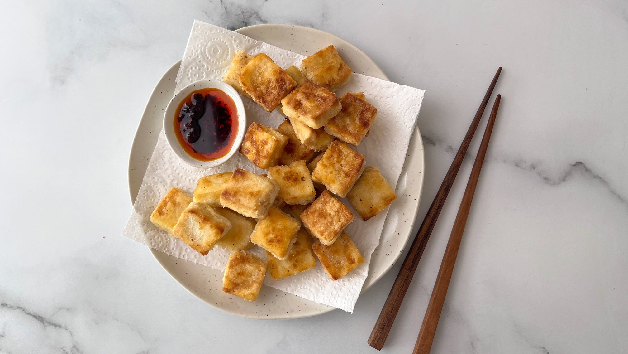Crispy fried cubed foods on paper towel lined plate with a small bowl of chilli oil. Chopsticks next to it.