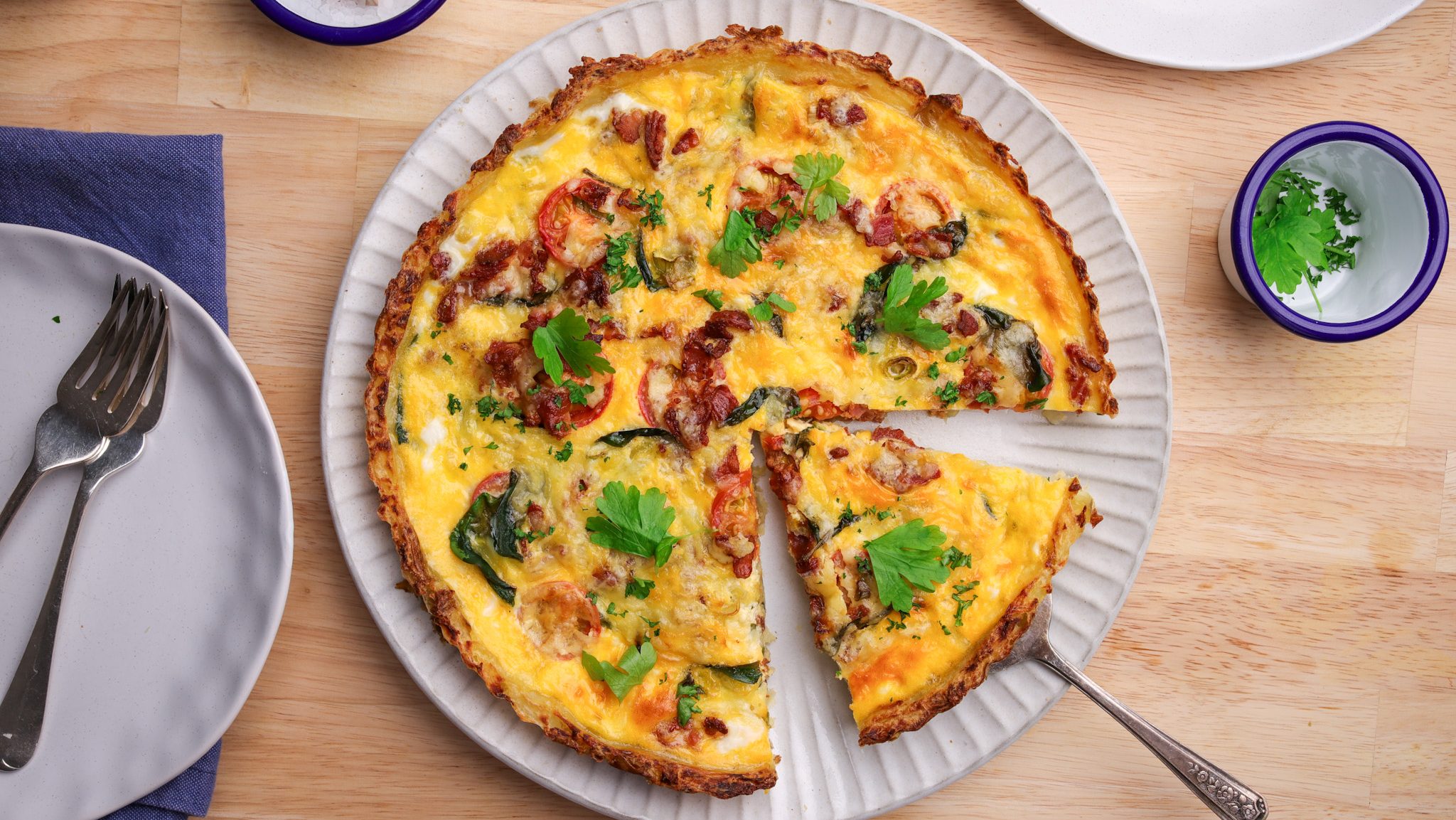 Baked quiche with pink bacon bits and herbs, a wedge sliced apart.