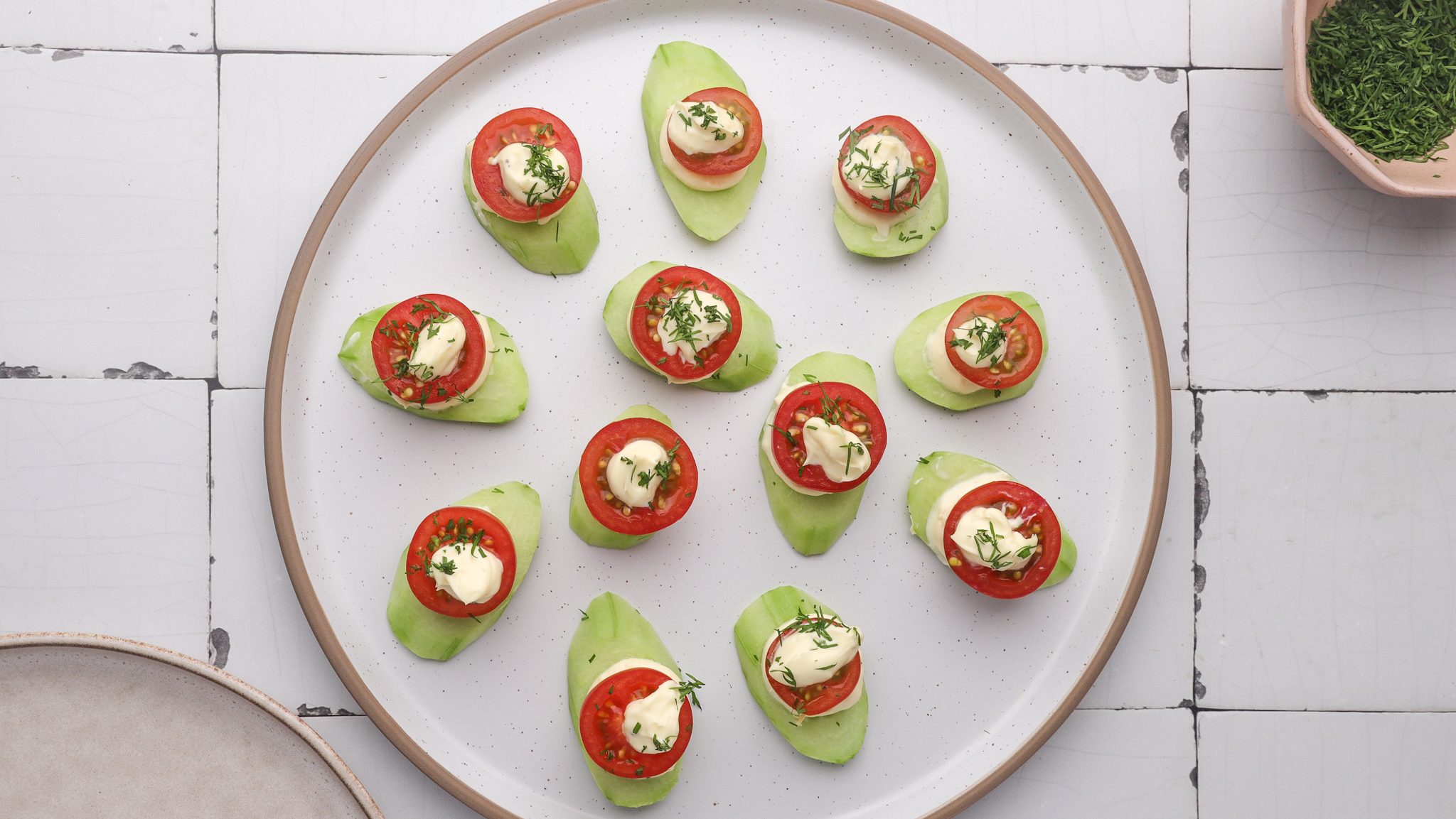 A topdown veiw of a white plate with cucumber, tomato and white cream canapes on it.