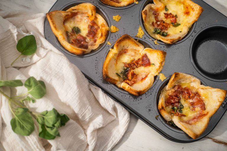 A six-hole muffin tin full of bread cup with pizza fillings and herb.