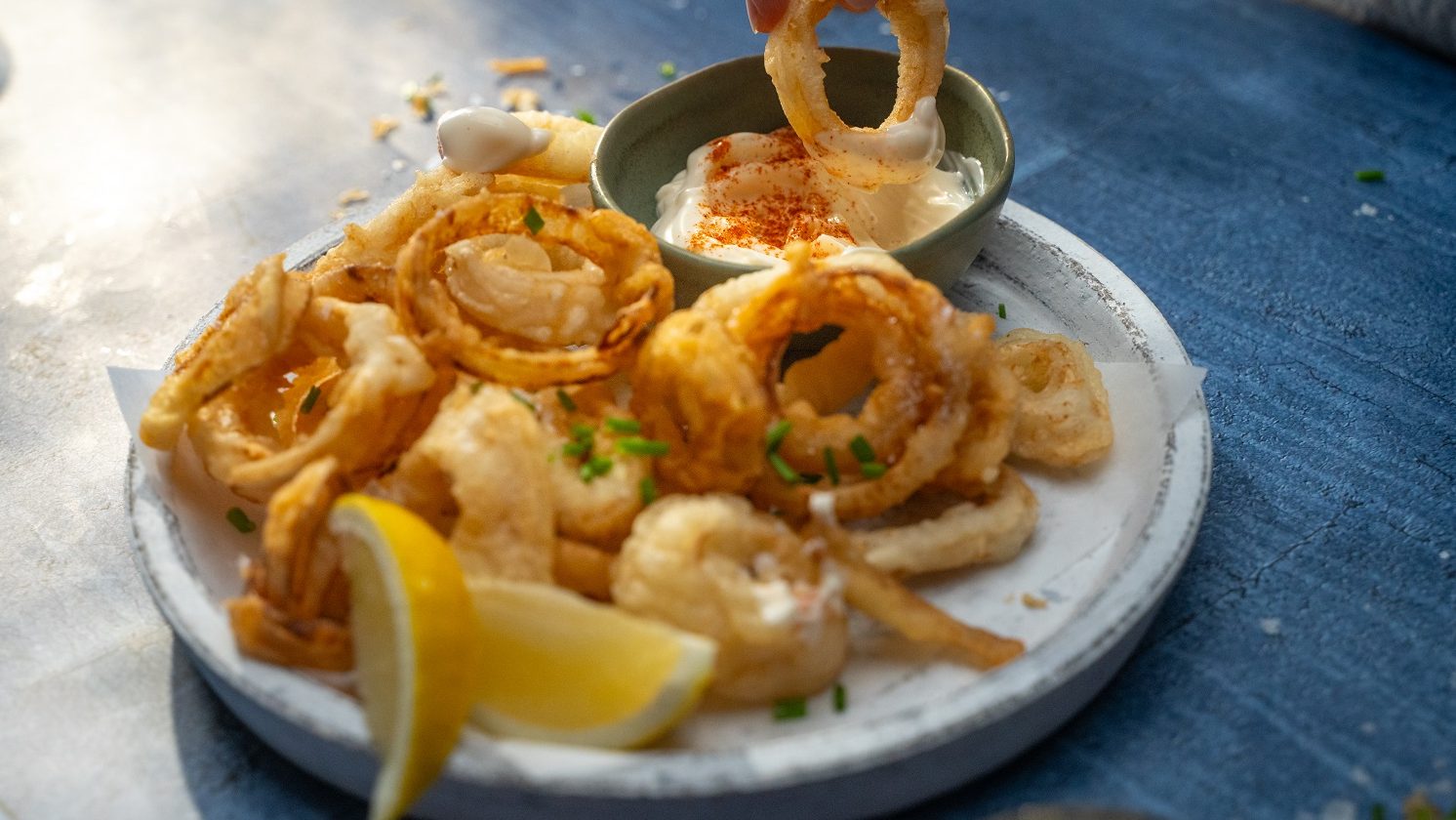 Plate of fried onion and squid rings with lemon wedges and a pot of dipping sauce.