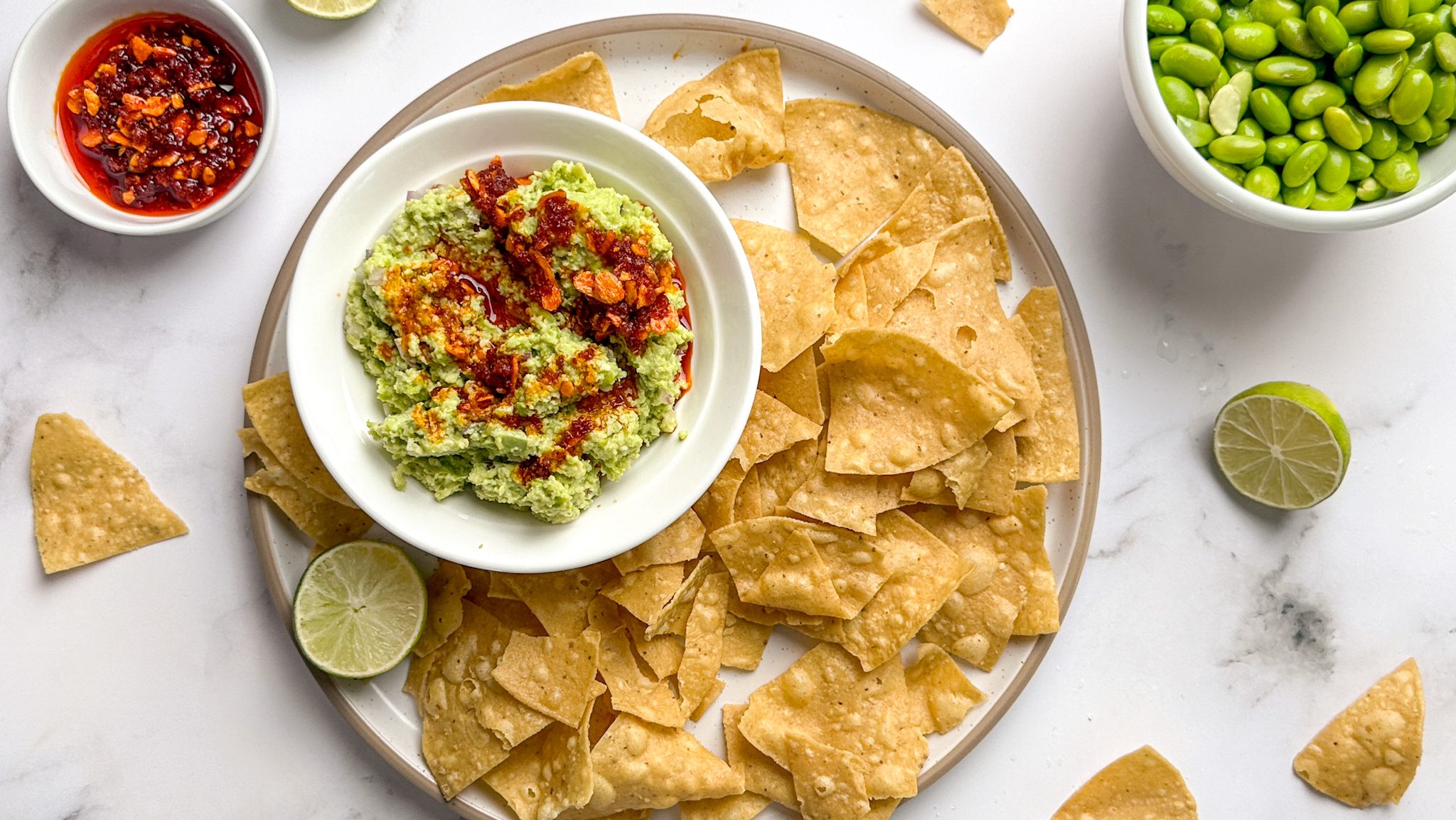 A plate of corn chips with a bowl of green dip topped with red sauce. Two bowls of red sauce and green beans.