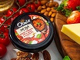 Pot of Obela Roasted Red Capsicum dip surrounded by tomatoes, cheese, nuts and strawberries.