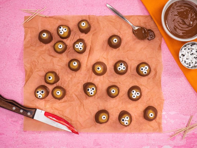 Chocolate dipped Halloween eyeballs treats on baking paper with a knife smeared with red jam.