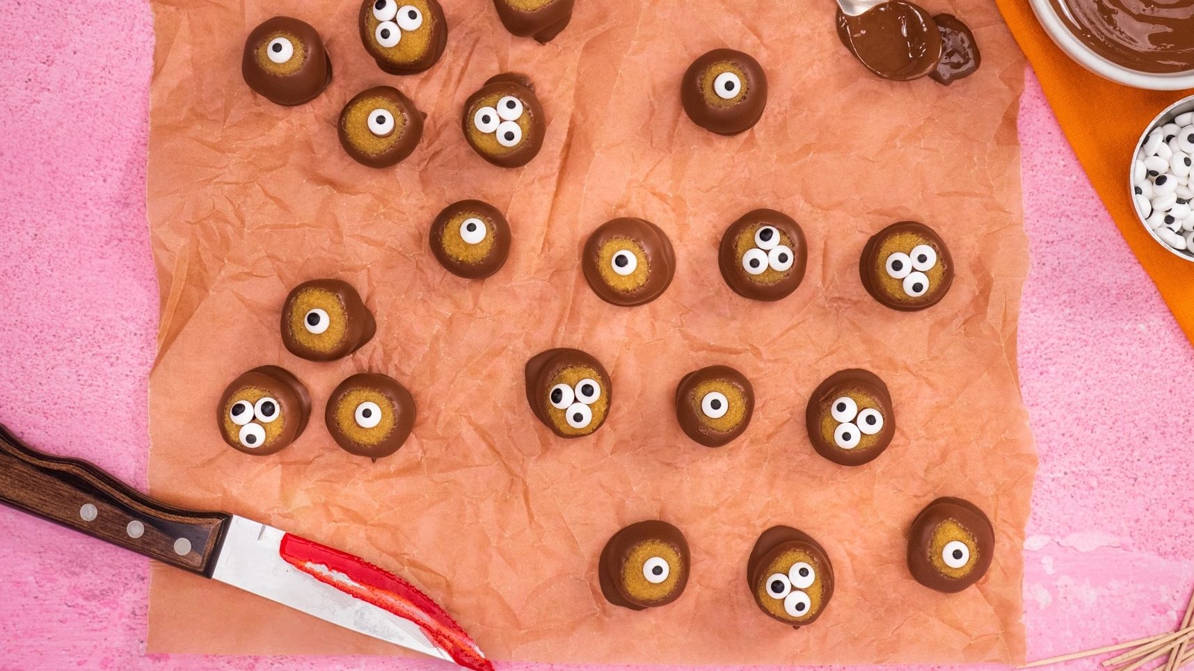 Chocolate dipped Halloween eyeballs treats on baking paper with a knife smeared with red jam.