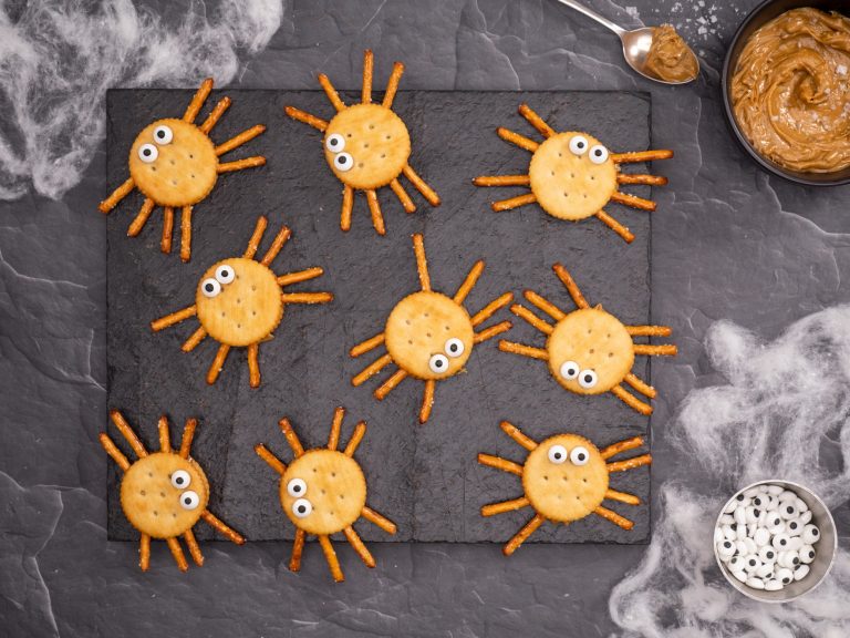 Nine cracker sandwich Halloween spiders with pretzel legs and candy eyes on slate
