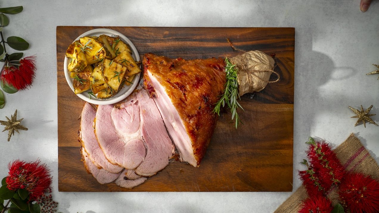 A baked glazed half leg ham, some slices showing inside. A bowl of cooked pineapple wedges.